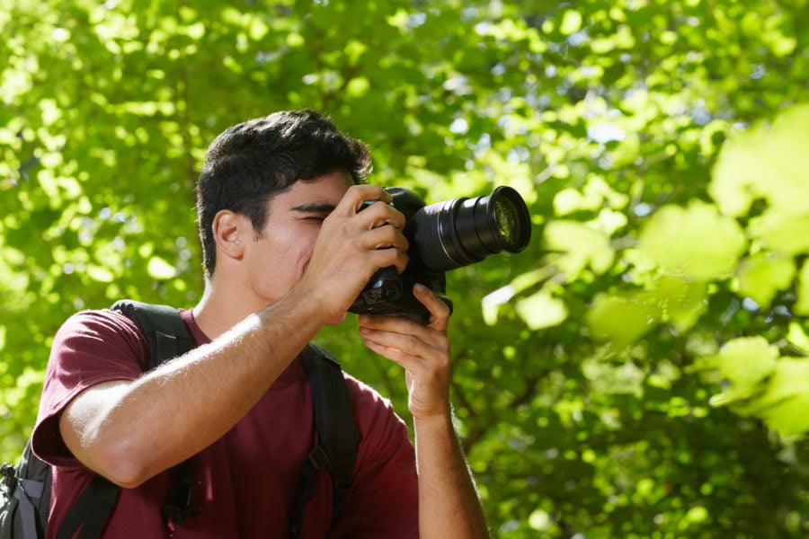 young hispanic man trekking among trees and taking pictures with dslr camera. Horizontal shape, side view, copy space